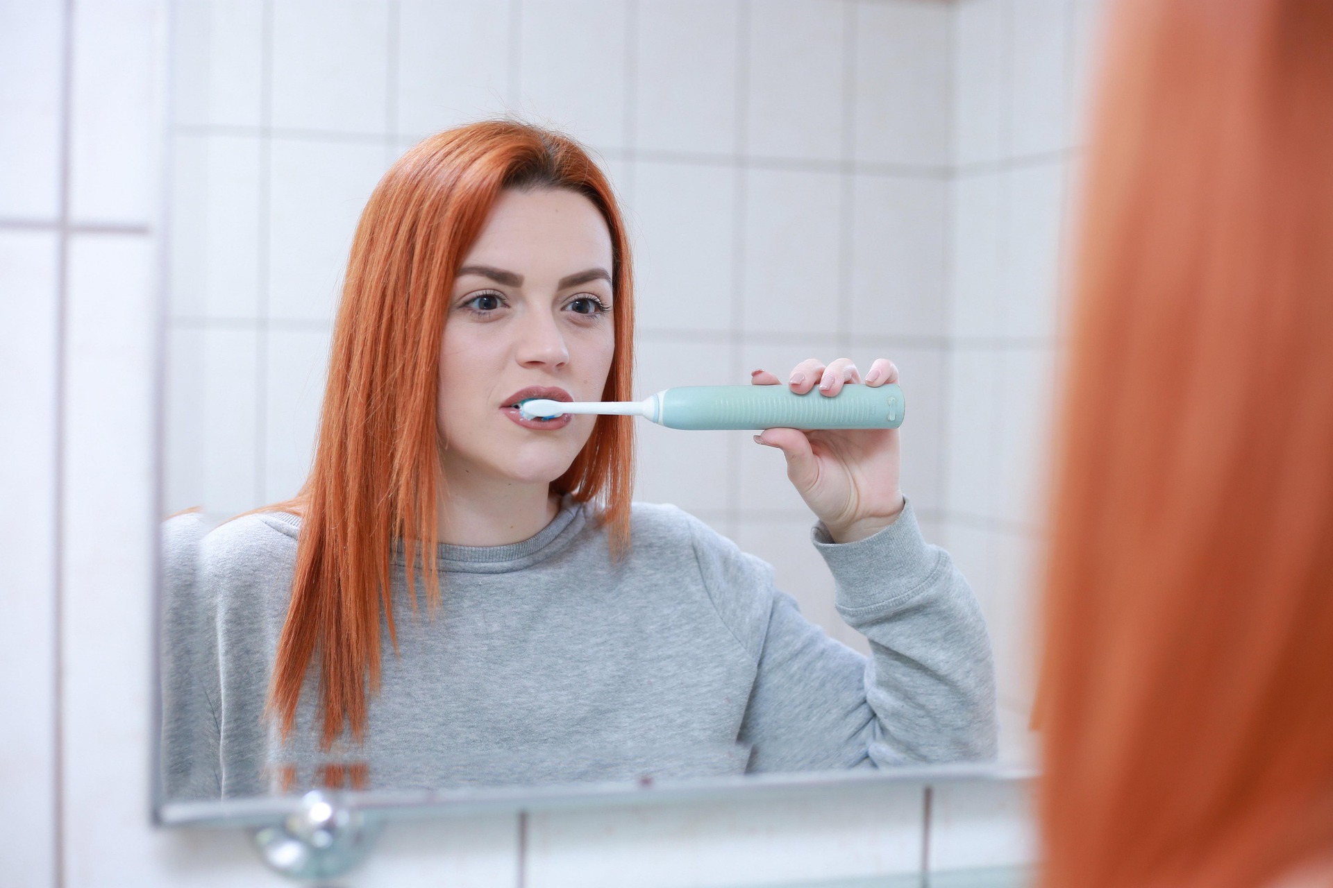 Woman brushing her teeth in the mirror.
