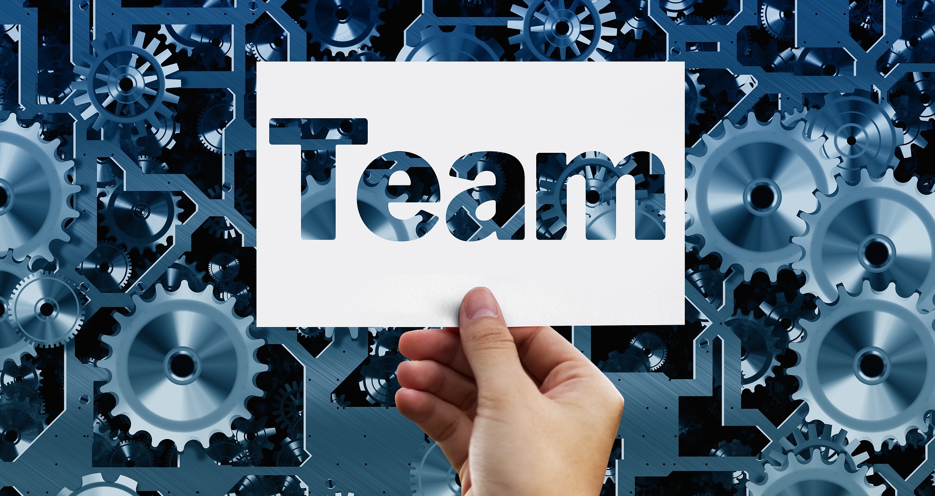 Holding a 'Team' sign with a background of machinery gears.