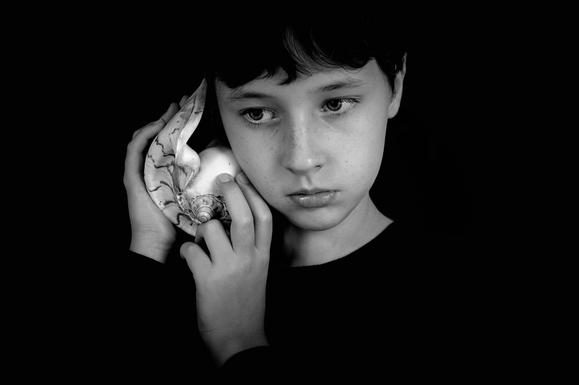 Young boy holding a large seashell up to his ear to listen.