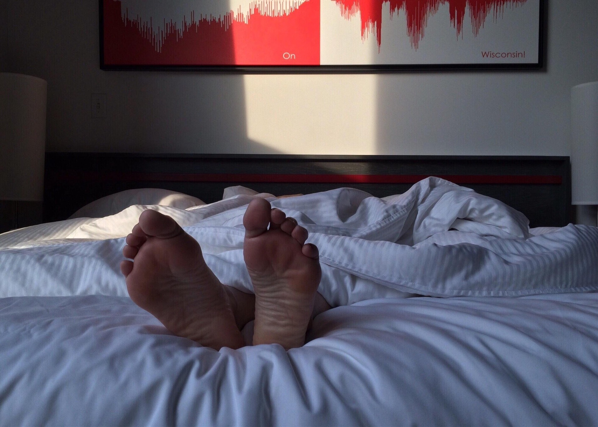 Sleepy person in bed under the comforter, just see their feet poking out.