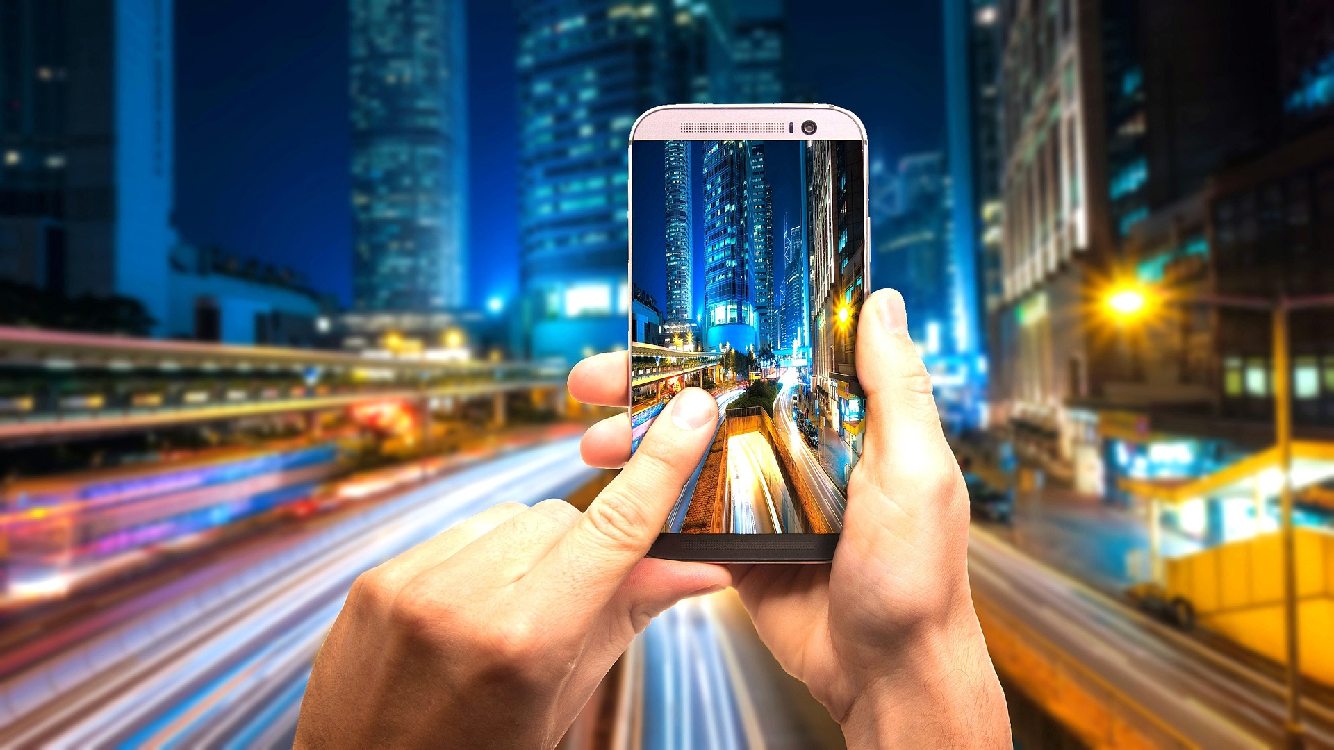 Taking a smart phone photo of a glowing cityscape at night.
