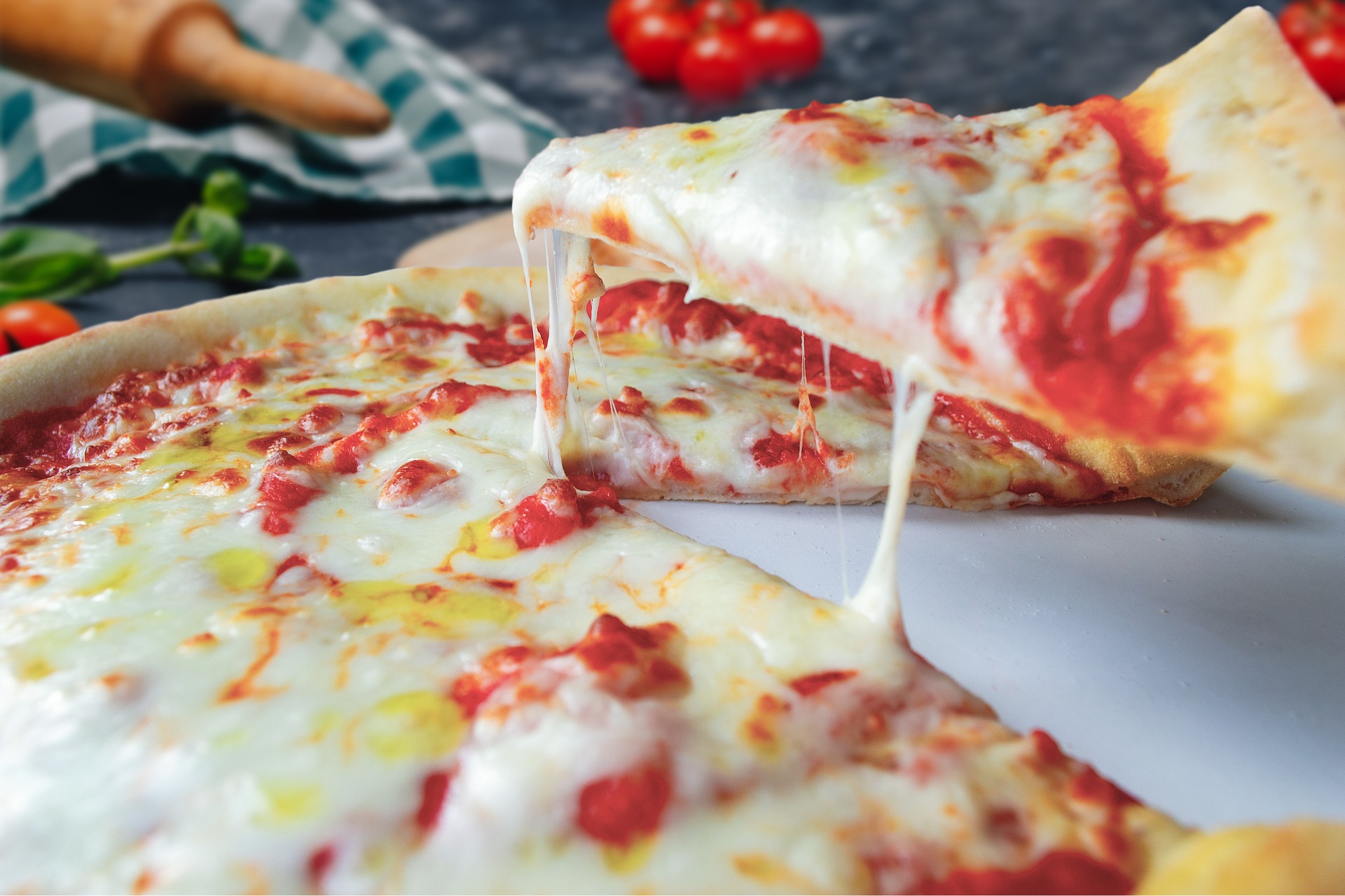 Lifting a slice of cheesy pizza from the pie.