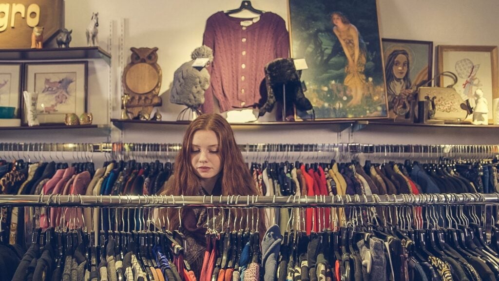 Younger girl shopping through racks of vintage clothes, thrifting.