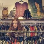 Younger girl shopping through racks of vintage clothes, thrifting.