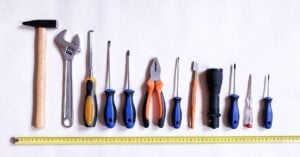A variety of tools from a toolkit, from tallest to shortest with a tape measure underneath.