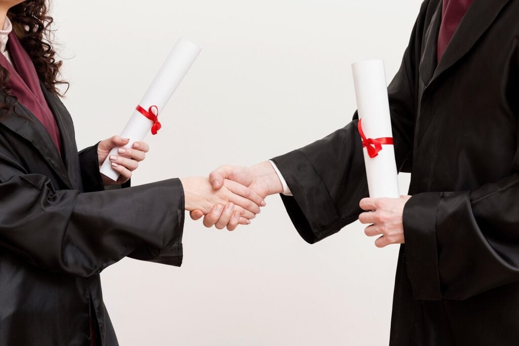 Graduation picture, shaking hands with diplomas, wearing gowns.
