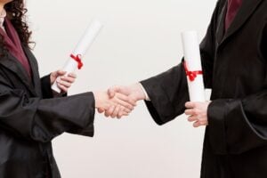 Graduation picture, shaking hands with diplomas, wearing gowns.