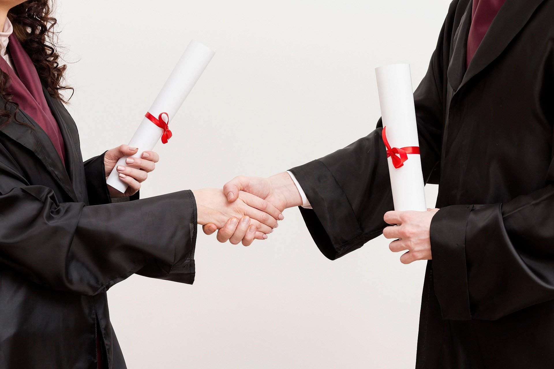 Graduation picture, shaking hands with diplomas, wearing gowns.