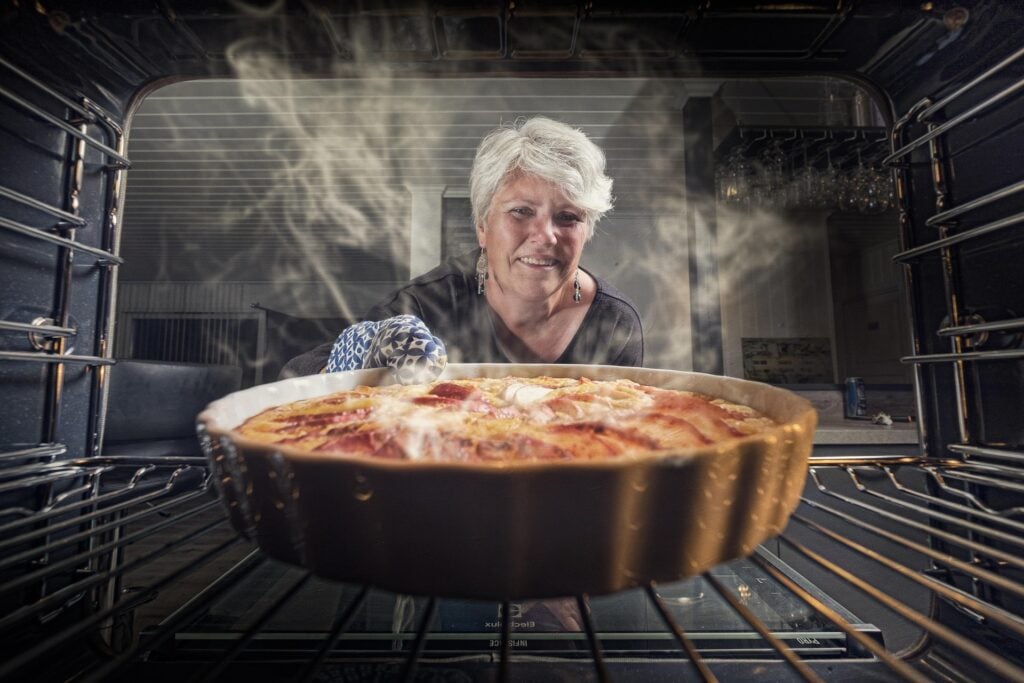 Older woman baking an apple pie in the oven in the kitchen.