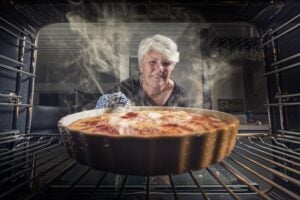 Older woman baking an apple pie in the oven in the kitchen.