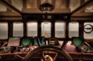 Steering helm at the center of a ship, with view out the windows.