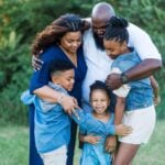 A happy family hugging each other in a circle outdoors, 3 kids and two adults.