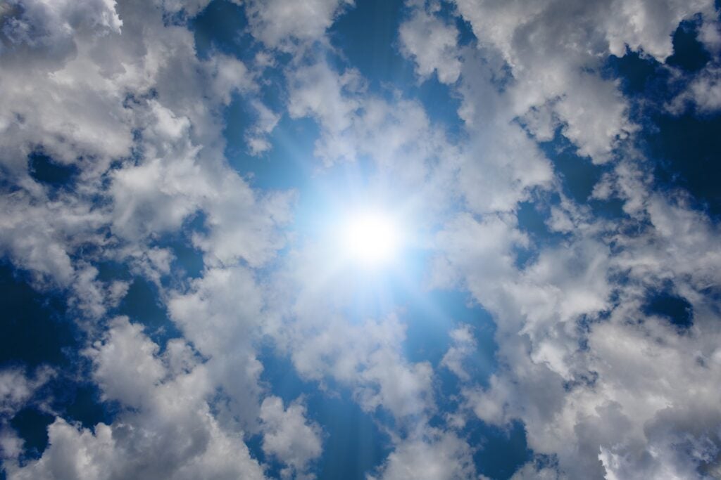 The sun high in the sky and rays of light shining through some clouds.