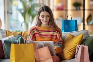Smiling female shopper at home on the laptop surrounded by shopping bags.