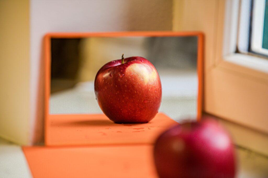A healthy-looking red apple reflected in a mirror.