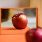 A healthy-looking red apple reflected in a mirror.