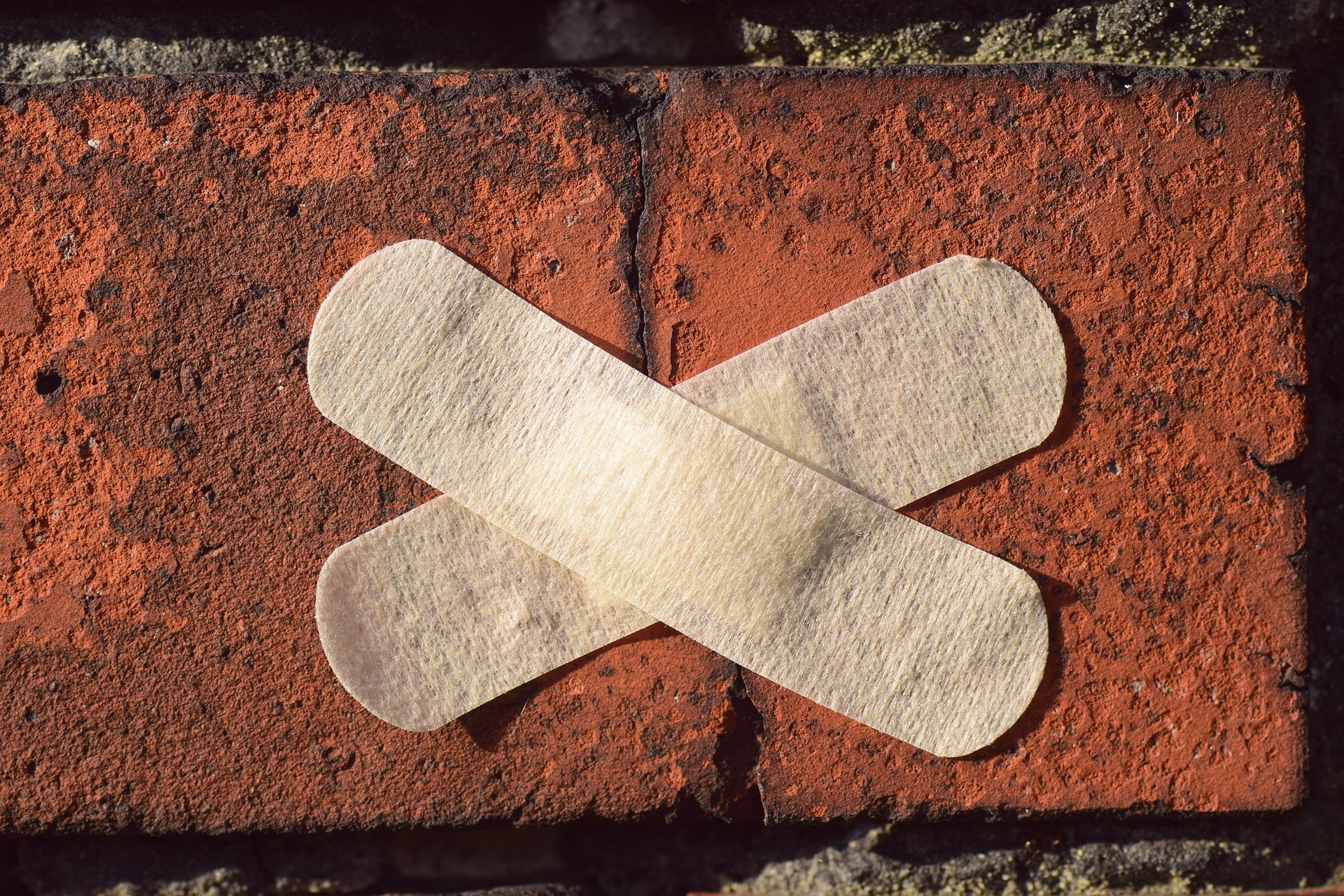 Red brick with crack with two band aids across it.