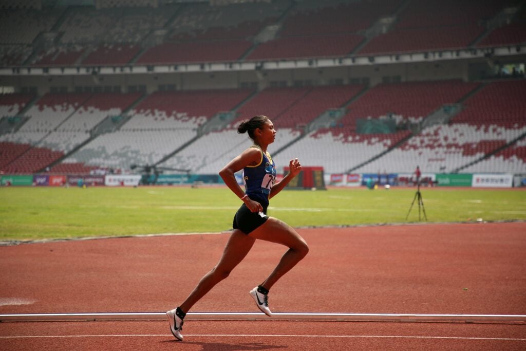 A woman marathon runner/athlete, taking a powerful stride on the racetrack.