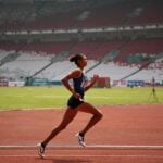A woman marathon runner/athlete, taking a powerful stride on the racetrack.