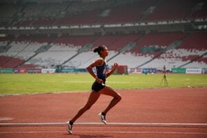 A woman marathon runner/athlete, taking a powerful stride on the racetrack.