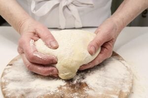A chef in the kitchen kneading a large piece of dough with flour on his hands.