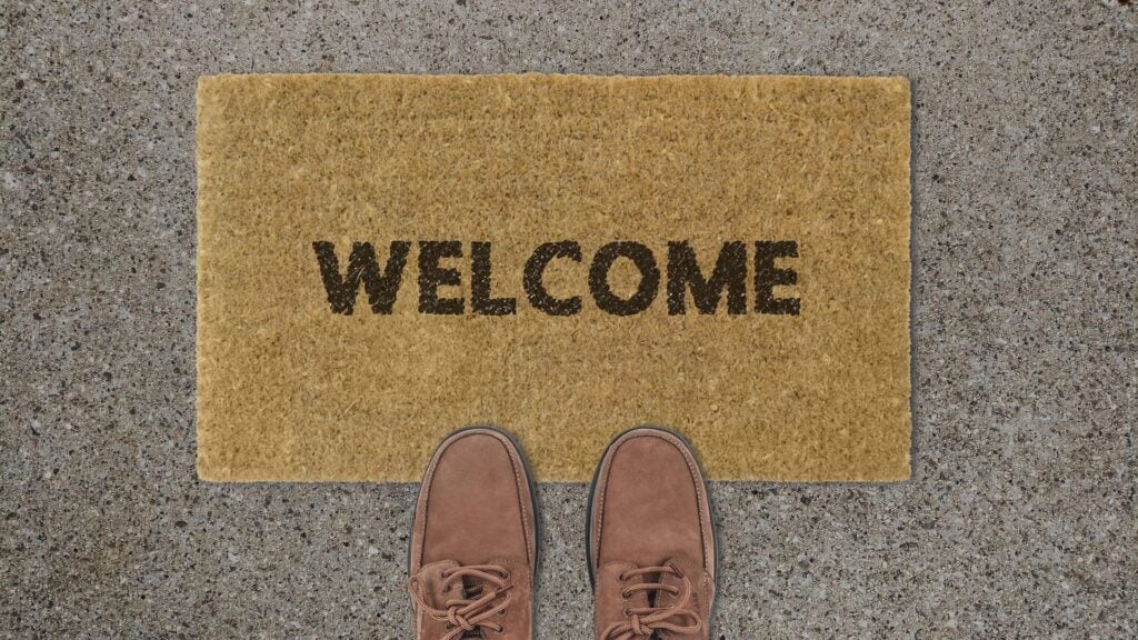 A welcome mat with shoes at the edge, like someone just about to walk in. Says 'Welcome.'