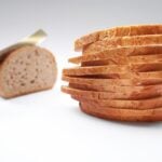 A knife slicing up a loaf of bread, with a big pile of differently sized slices.