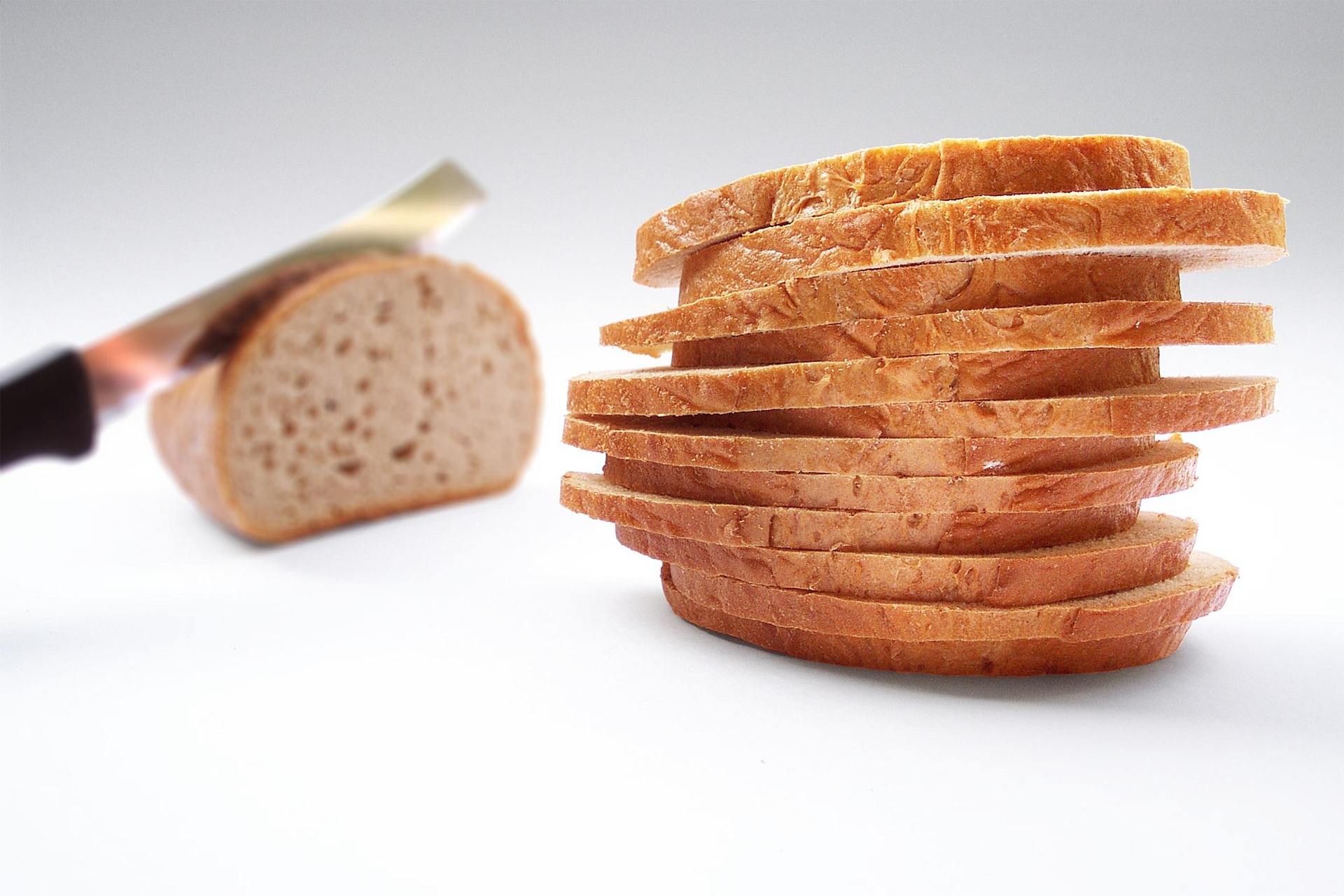 A knife slicing up a loaf of bread, with a big pile of differently sized slices.