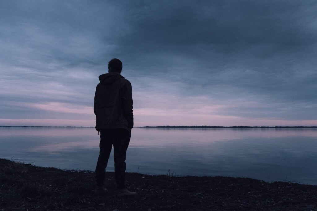 Silhouette of man by a lake as it gets dark, symbolizing the consumer for next year amid uncertainty.