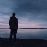 Silhouette of man by a lake as it gets dark, symbolizing the consumer for next year amid uncertainty.