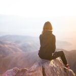 Woman sitting on mountain top, looking off into the distance.