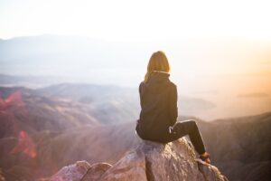 Woman sitting on mountain top, looking off into the distance.