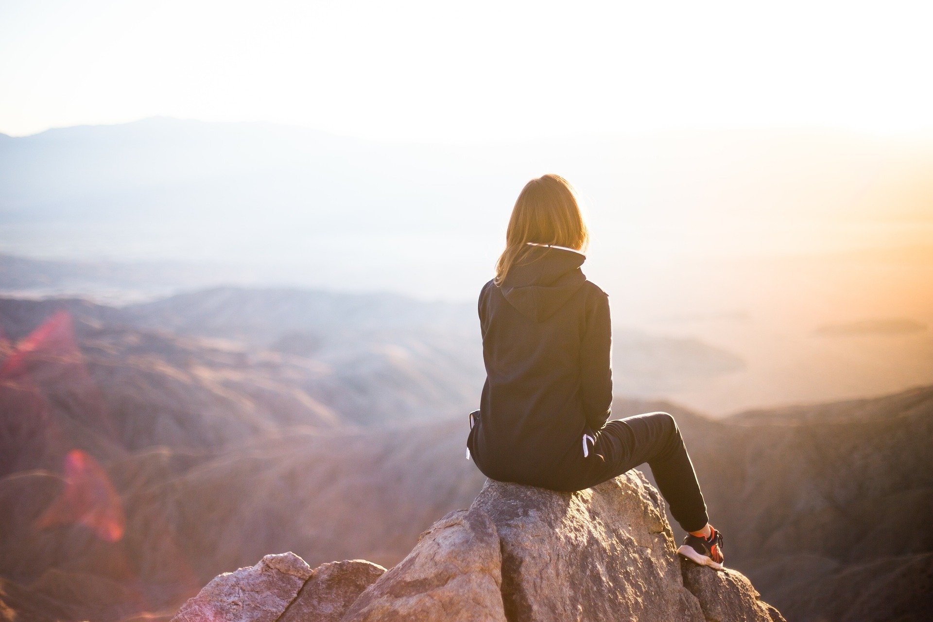 Woman sitting on mountain top, looking off into the distance.