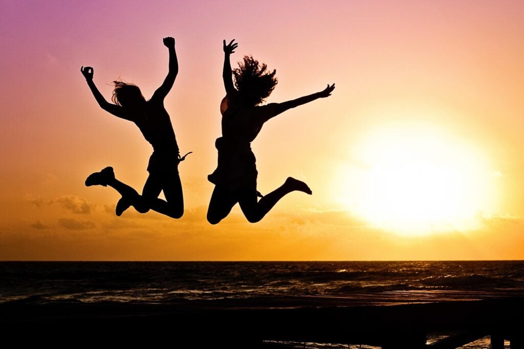 Silhouettes of two women jumping joyously in the air during a sunrise/sunset.