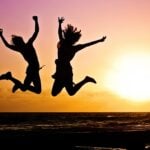 Silhouettes of two women jumping joyously in the air during a sunrise/sunset.