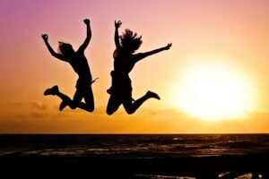 Silhouettes of two women jumping joyously in the air during a sunrise/sunset.