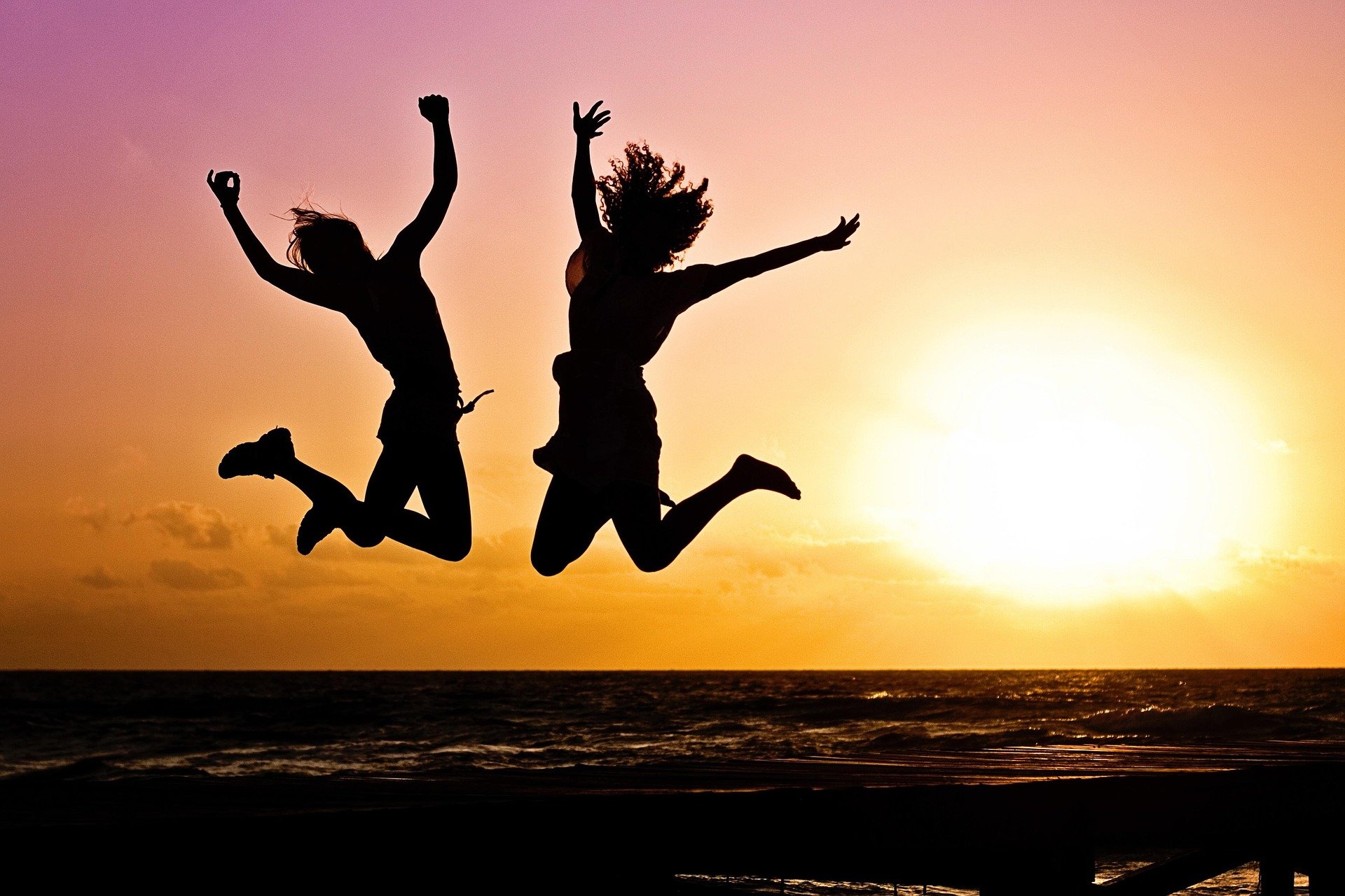 Silhouettes of two women jumping joyously in the air during a sunrise/sunset.
