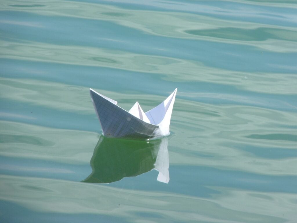 A lone small paper boat, floating in water, waves slowly rippling.