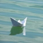 A lone small paper boat, floating in water, waves slowly rippling.