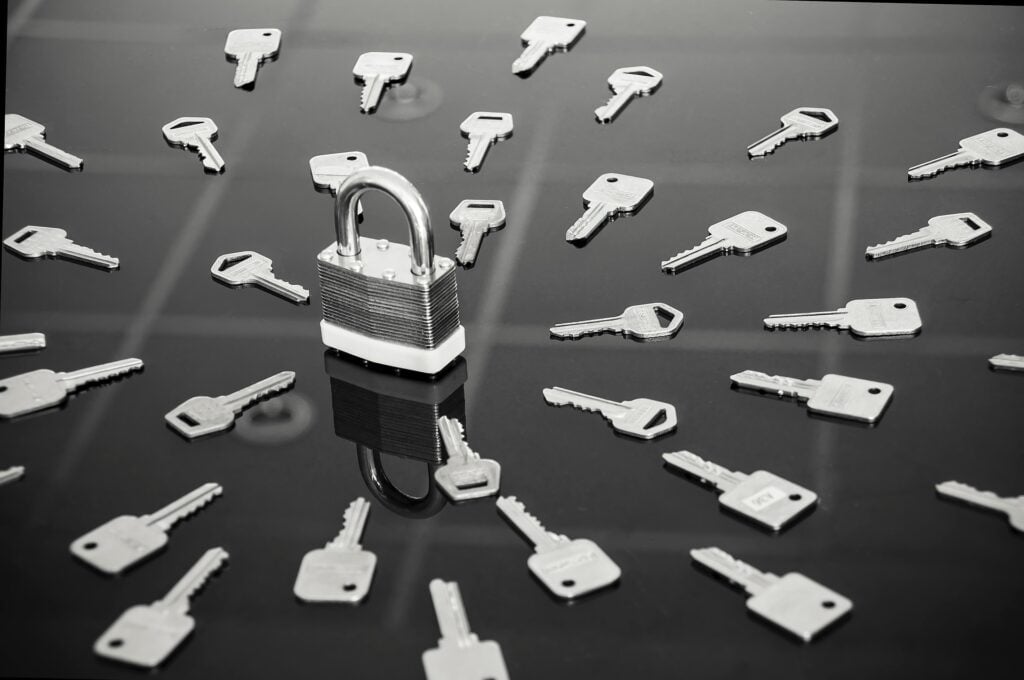 A black and white image showing a padlock surrounded by a grouping of keys.