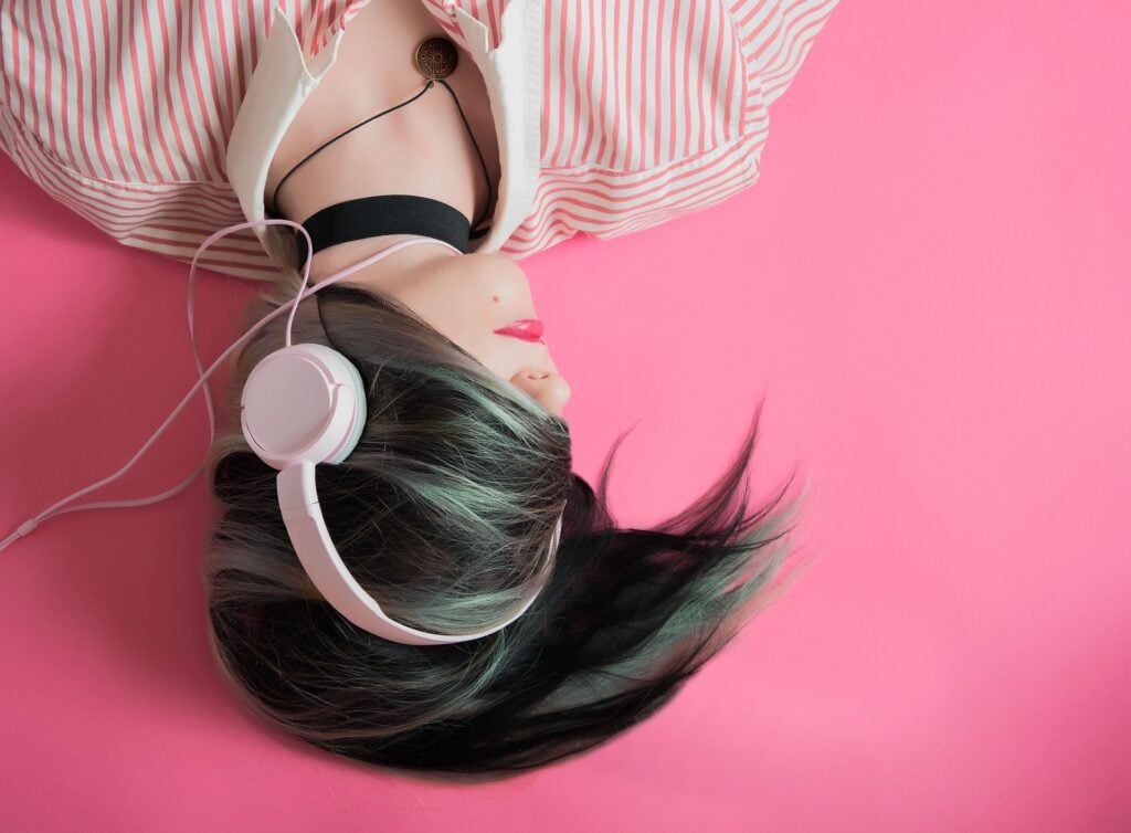 Young teenage girl, lying upside down to the viewer, with hair across her face and listening to music with headphones.