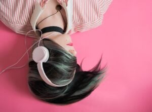 Young teenage girl, lying upside down to the viewer, with hair across her face and listening to music with headphones.