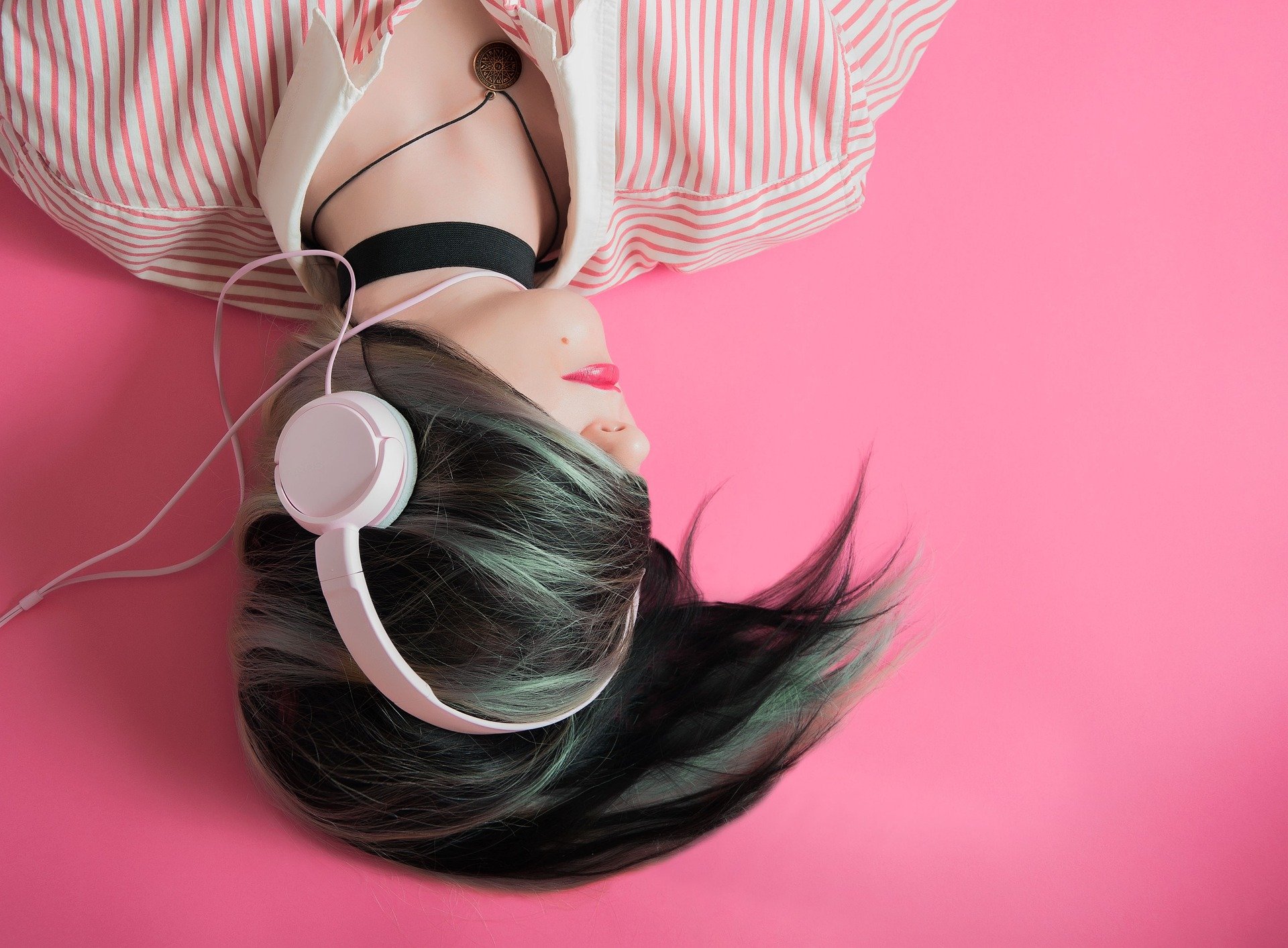 Young teenage girl, lying upside down to the viewer, with hair across her face and listening to music with headphones.