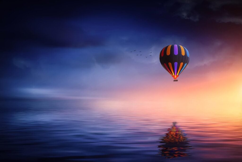 A colorful hot air balloon in the distance floating above a lake.