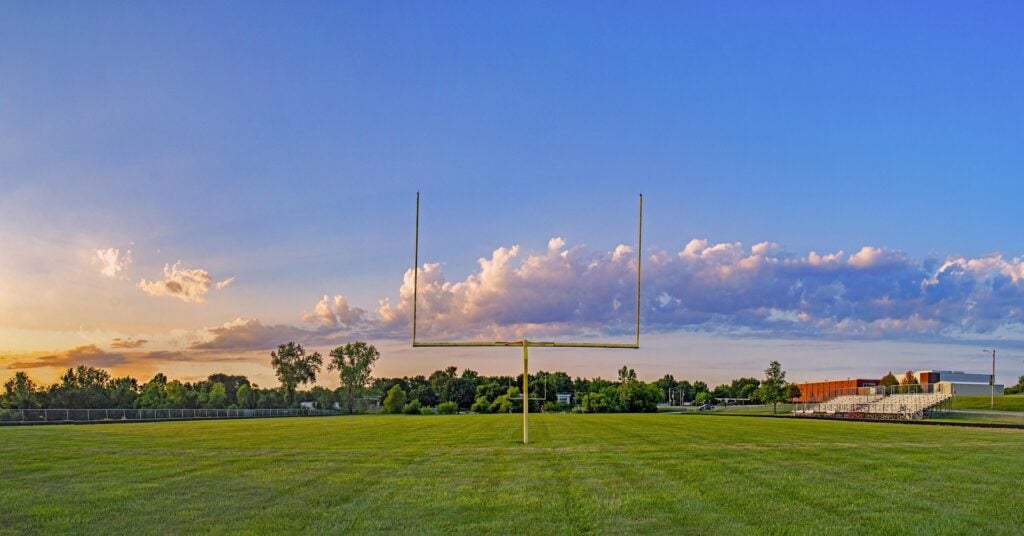 Football field goal post on a green football field, blue skies and athletic field background.