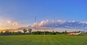 Football field goal post on a green football field, blue skies and athletic field background.