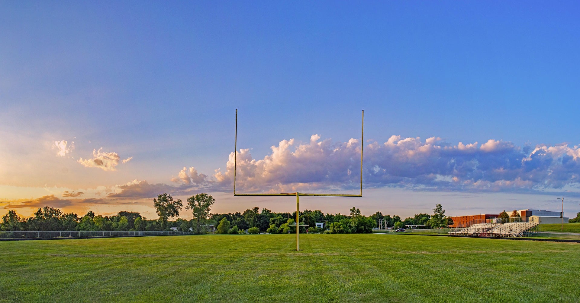 Football field goal post on a green football field, blue skies and athletic field background.