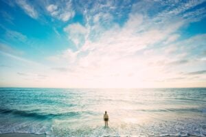 Woman standing in the water at the beach surf, looking out into wide horizon/ocean.