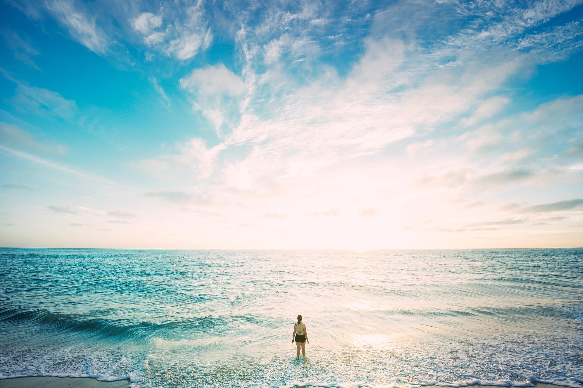 Woman standing in the water at the beach surf, looking out into wide horizon/ocean.