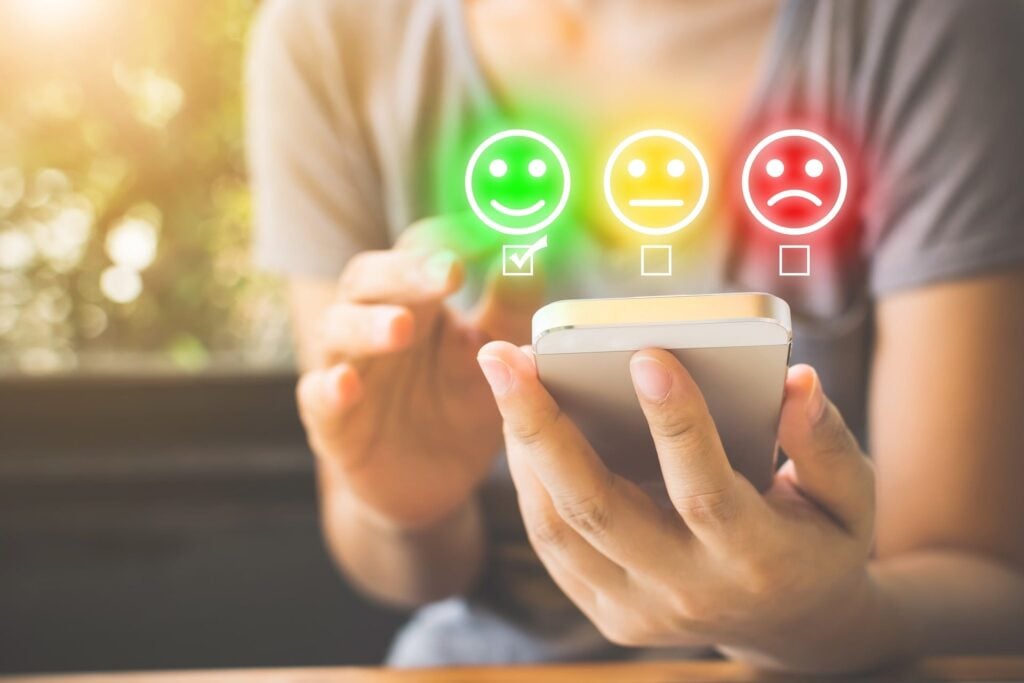 Consumer on their smartphone showing customer service icons, such as smiley face to neutral to sad face.